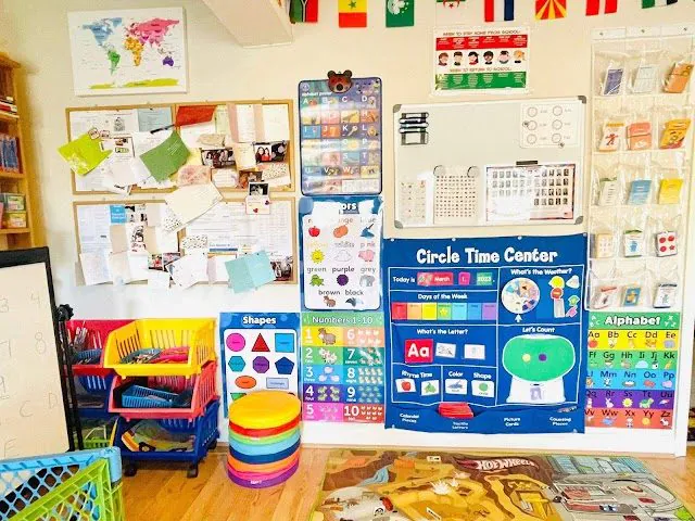Childcare classroom wall with a circle time chart, alphabet and number posters, a world map and seat cushions