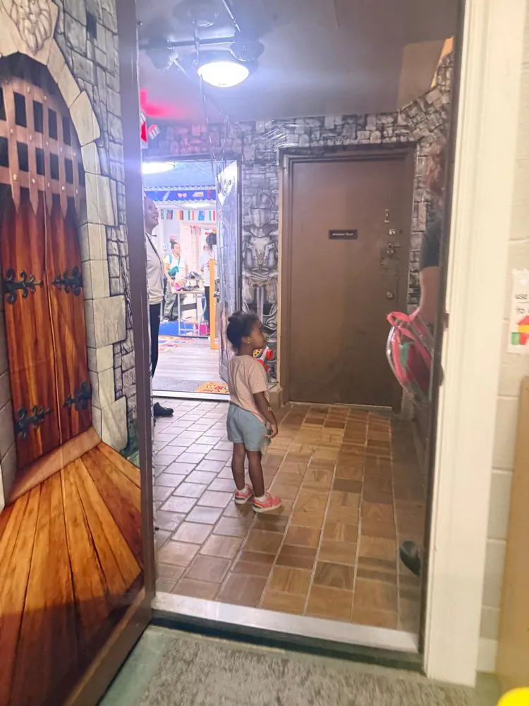 A toddler steps through EduCastle&rsquo;s painted castle-gate entrance into a stone-themed hallway leading to a classroom
