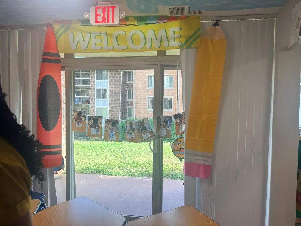 Classroom glass door at EduCastle with a &ldquo;Welcome&rdquo; banner, giant crayon and pencil decorations and children&rsquo;s artwork