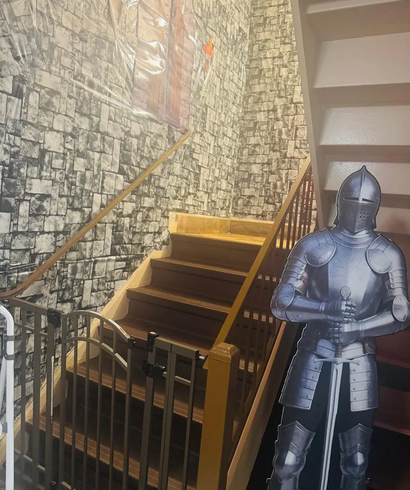 A life-size knight cutout stands beside a gated staircase with stone-wall murals at EduCastle