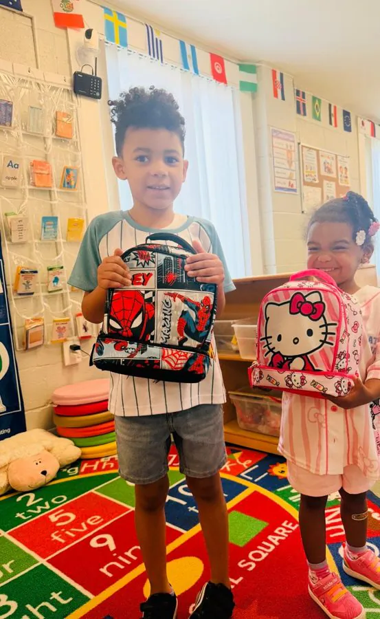 Two cheerful preschoolers proudly hold up their character lunchboxes in a bright EduCastle classroom