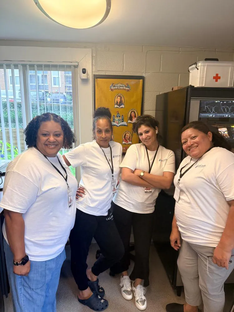 Four smiling EduCastle teachers in matching white shirts and ID lanyards posing in the front office