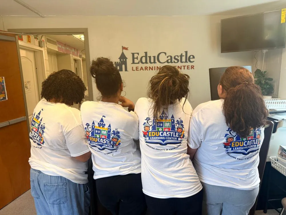 Four EduCastle teachers seen from behind in matching &ldquo;Creating Knights of Knowledge&rdquo; open house shirts