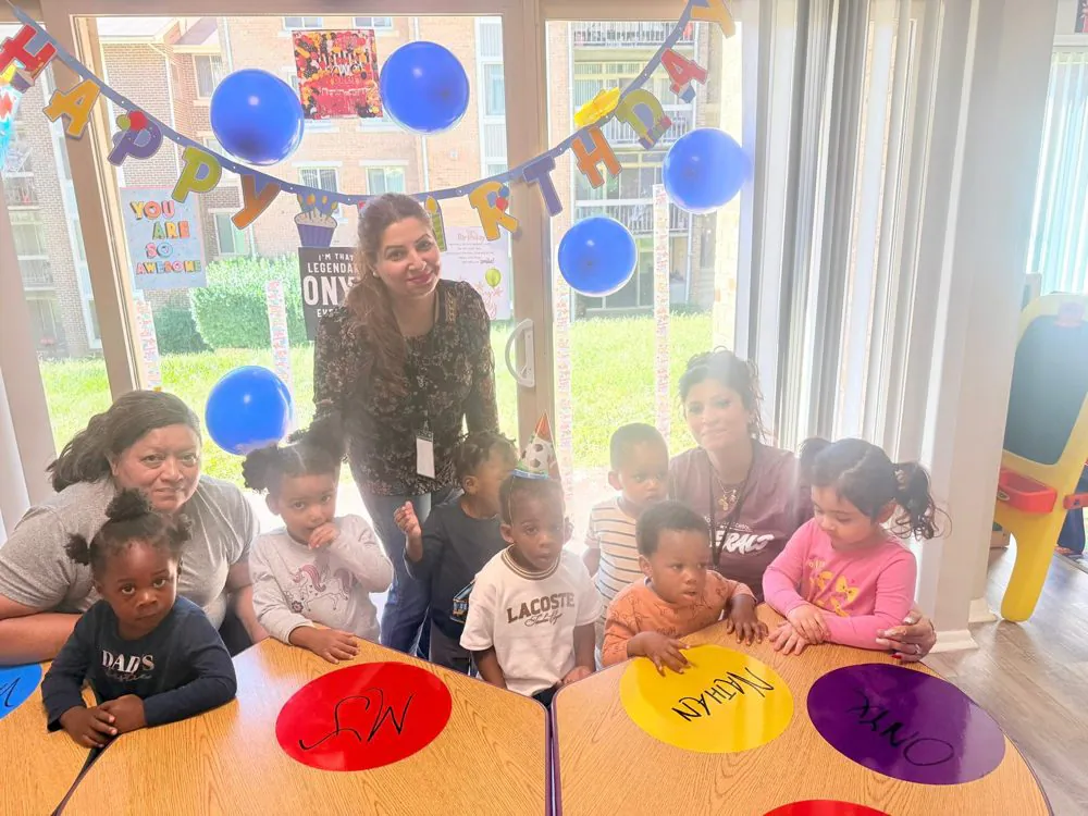 EduCastle teachers with toddlers at a birthday party, under blue balloons and a Happy Birthday banner